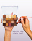 Hand holding a FIXY small clear makeup palette, filled with colorful eyeshadows and a brush applying makeup, demonstrating the palette's convenient size that fits in the palm of your hand for easy use and portability.
